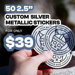 Marketing image showing reflective silver metallic stickers with Viking-themed artwork. A hand displays multiple stickers to highlight the metallic finish. Large text advertises 50 custom 2.5-inch silver metallic stickers for $39.