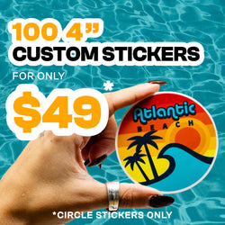 Hand holding a round Atlantic Beach sticker featuring a stylized sunset with warm gradient stripes, palm trees, and an ocean wave illustrated in a bold retro surf-graphics style. Background shows rippling turquoise water. On-image text reads 100 4 inch custom stickers for 49. Keywords: beach sticker, retro surf art, coastal vinyl decal, circle sticker design.