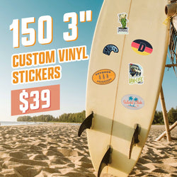 Surfboard standing in sand with multiple stickers applied: a green fish labeled Drum Trout, a zebra-patterned wave, an oval Germany-inspired D sticker, an orange Outdoor Adventure University badge with pine trees, a Van Life illustrated camper van, and a blue Island Club palm tree logo. Ocean and blue sky in background. On-image text 150 3 inch custom vinyl stickers and 39. Keywords: surfboard stickers, beach lifestyle decals, travel vinyl graphics.