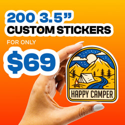 Hand holding a large vinyl sticker showing mountains, a tent, a flowing river, stars, and the printed text Happy Camper in bold lettering. Gradient orange background. On-image text reads 200 3.5 inch custom stickers for $69. Camping sticker design ideal for outdoor decal, hiking sticker, and adventure vinyl sticker keywords.