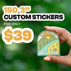 Promotional graphic featuring a hand holding a retro-style illustrated sticker for Big Bend Nat’l Park. The sticker artwork shows a warm, vintage-inspired landscape with stylized mountains, tall pine trees, a winding river, and a golden rising sun, all in muted greens, yellows, and oranges. The background is soft, blurred green foliage that creates an outdoor, nature-themed atmosphere. Text on the graphic reads 150 3” custom stickers and for only $39 in bold white, black, and golden-yellow lettering