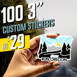 Hand holding a die cut Oregon-shaped sticker with mountains, sunrise rays, evergreen trees, winding road, and text Run Oregon with ASICS logo. Forest road backdrop. On-image text 100 3 inch custom stickers and 29. Keywords: running sticker, state outline decal, Oregon outdoor sticker.