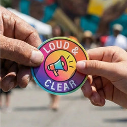 Two hands exchange a colorful round sticker featuring a megaphone graphic and the words 