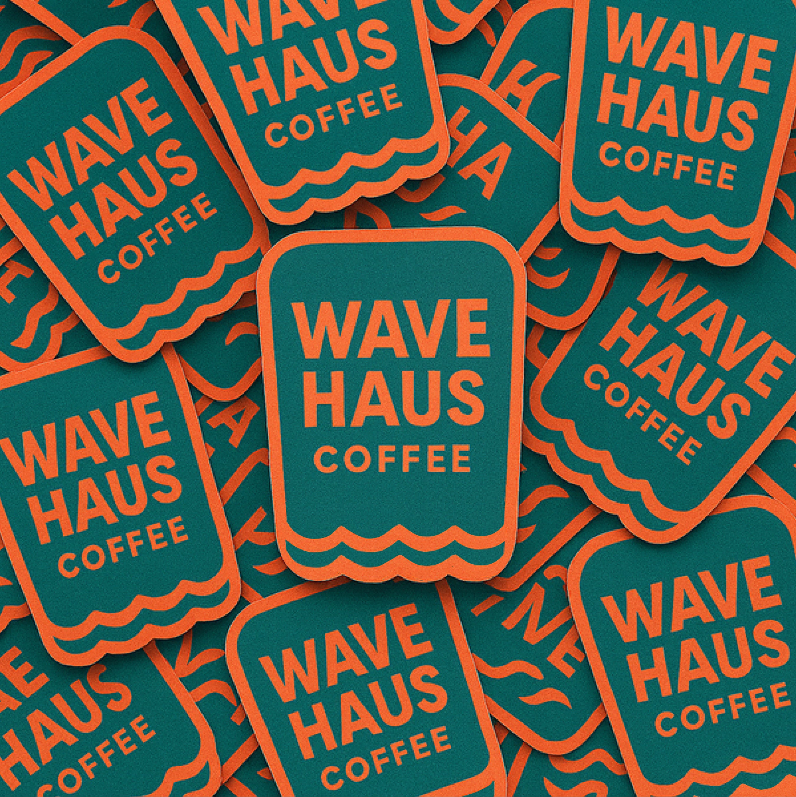 A pile of Wave Haus Coffee branded stickers or labels with a teal background, orange border, and orange text reading 'WAVE HAUS COFFEE'.