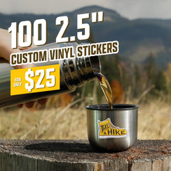 Metal camping cup with a yellow boot sticker reading Take a Hike while coffee is poured from a thermos on a tree stump in a mountainous outdoor setting. On-image text reads 100 2.5 inch custom vinyl stickers for $25. Keywords: hiking stickers, camping decals, adventure vinyl sticker art.