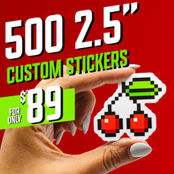 Hand holding a die-cut sticker of two pixel-art cherries with emerald green stems against a bright red background. The sticker features retro 8-bit digital style reminiscent of classic arcade graphics. On-image text reads 500 2.5 inch custom stickers and 89. Keywords: pixel art sticker, retro gaming decal, 8-bit cherries design, aesthetic vinyl sticker.