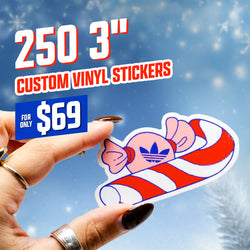 Image displaying text 250 3 inch custom vinyl stickers and 69 dollars. A hand holds a die cut sticker of a pink wrapped candy featuring a blue trefoil emblem resting on a red-and-white striped candy cane. Snowy winter background with soft bokeh lighting. Festive cartoon aesthetic waterproof sticker.