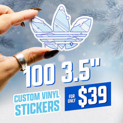 Hand holding a die-cut sticker shaped like a three-petal crest, illustrated in cool winter blues with minimalist mountain peaks, snow caps, and geometric line details. Art style blends modern vector minimalism with a tech-inspired aesthetic. Frosted blue background with soft snowflake bokeh. On-image text reads 100 3.5 inch custom vinyl stickers and 39. Keywords: winter mountain sticker, minimal line-art decal, geometric vector vinyl sticker.