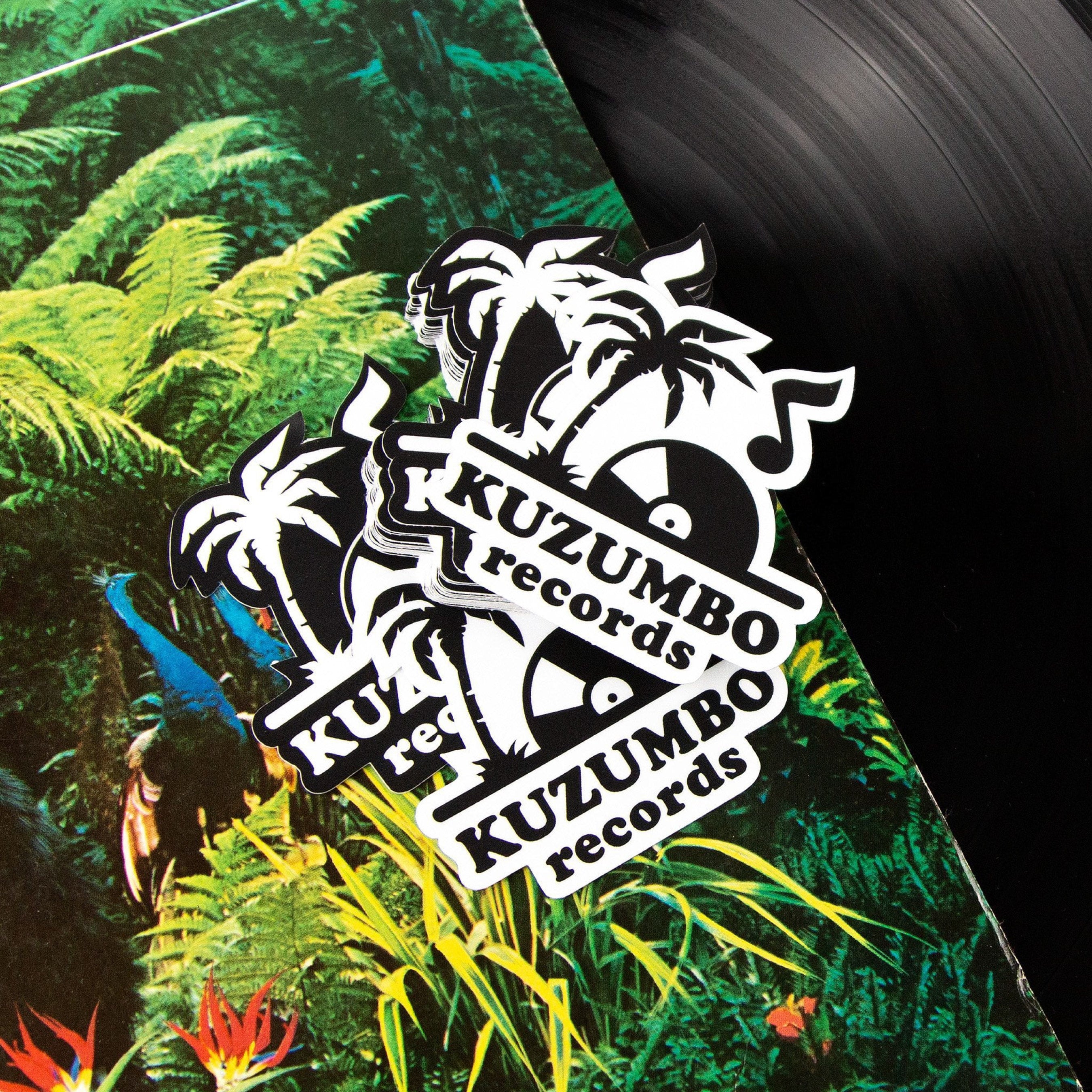 Stack of black-and-white custom die-cut vinyl stickers displayed on a vinyl record and tropical album artwork. The sticker features palm trees, a vinyl record graphic, and the text "KUZUMBO records." The durable custom logo stickers showcase crisp detail, bold contrast, and clean die-cut edges for music labels, bands, record stores, promotional branding, and merchandise.