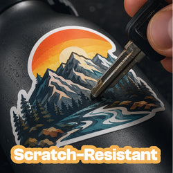 A close-up of a black insulated bottle with a colorful mountain-and-river sticker, being scratched with a metal key. The sticker is partially covered by an orange label reading 'Scratch-Resistant'.