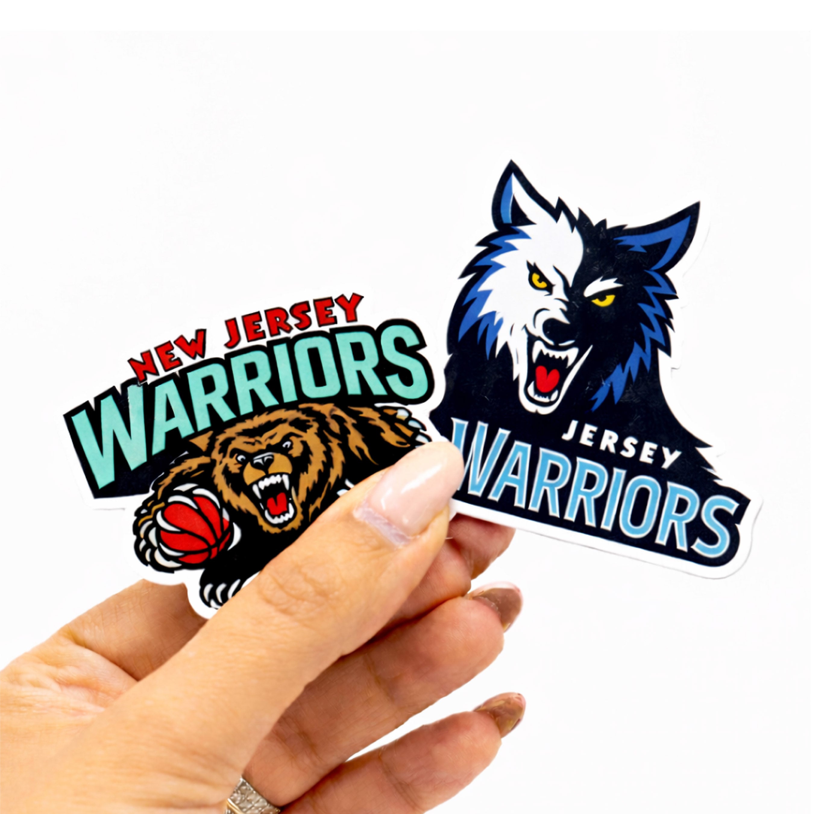 Two New Jersey Warriors die-cut stickers held by a hand against a plain white background. One sticker features a snarling wolf head with blue, white, and black details, and the other features a snarling bear holding a basketball with teal, red, and black lettering.