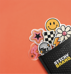 A black textured pouch with 'STICKY BRAND' printed in white and yellow sits on a solid orange background, partially filled with colorful novelty stickers including a smiley face, disco ball, flower, checkered flag, pink star, and lightning bolt.