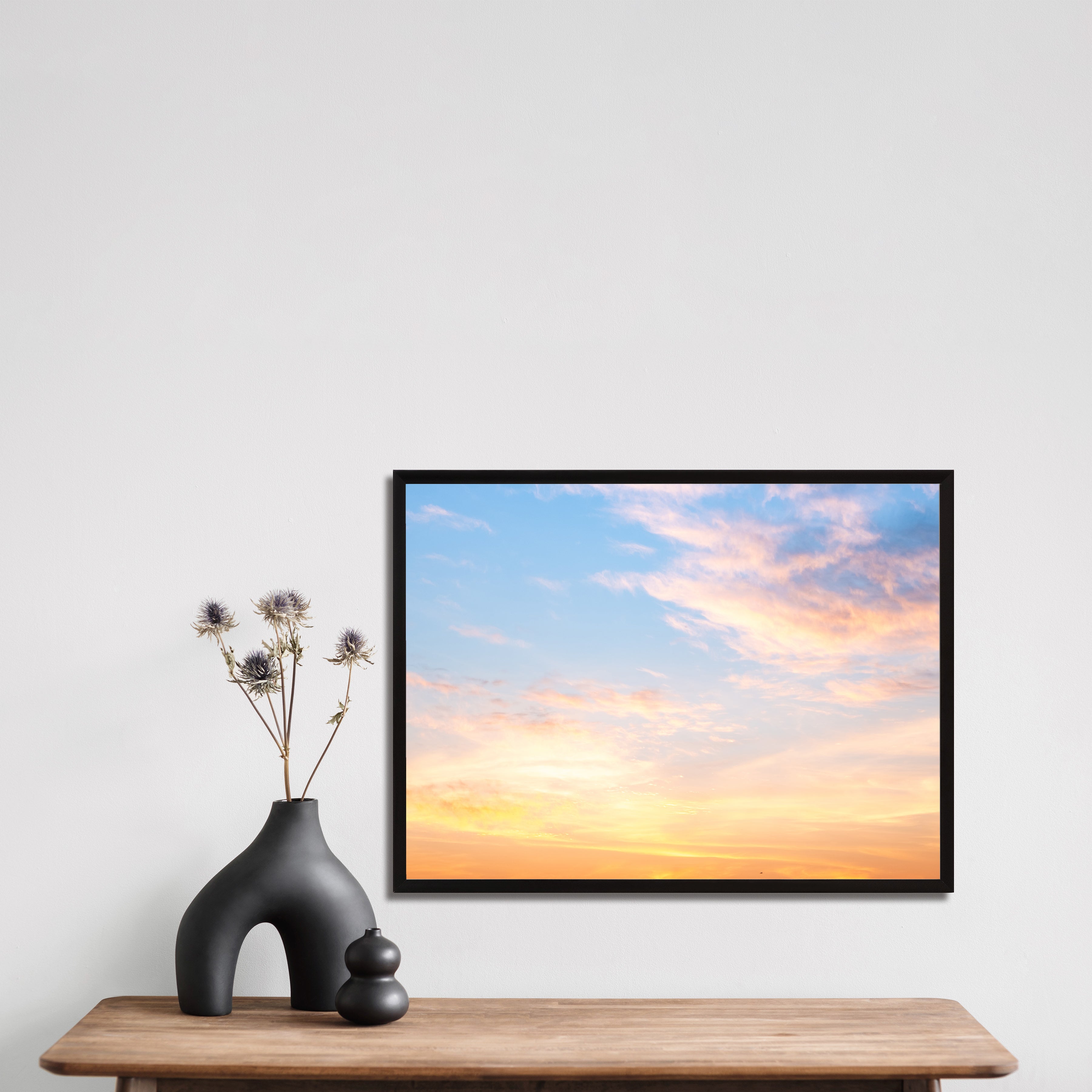 Framed canvas artwork of a sunset with a vase and decorative items on a table.