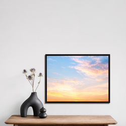 Framed canvas artwork of a sunset with a vase and decorative items on a table.