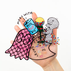 A hand holding several overlapping clear vinyl stickers against a white background. The stickers feature playful illustrated designs including a pink patterned ghost, a soda can labeled Real Pop with the phrase Made with Real Pop, a gumball machine character spilling colorful gumballs, and layered text reading Support Your Local Ground Snacks in multicolored lettering.
