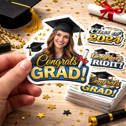 Hand holding a custom graduation sticker featuring a smiling graduate in cap and gown with Congrats Grad text. Surrounding scene includes stacked stickers, confetti, diploma, graduation cap, and Class of 2024 designs on a wooden table, creating a celebratory graduation party setting
