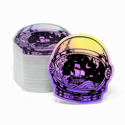 Holographic sticker of an astronaut helmet with a ship design, next to a stack of similar stickers. Rainbow iridescent sailboat waves maritime