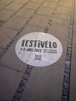 Sidewalk decal advertising a music festival used as temporary promotional signage. black and white sidewalk decal reads. Festivelo 1-2 Juli 2022 Musik. Storskaerm. Mad. Faelledparken