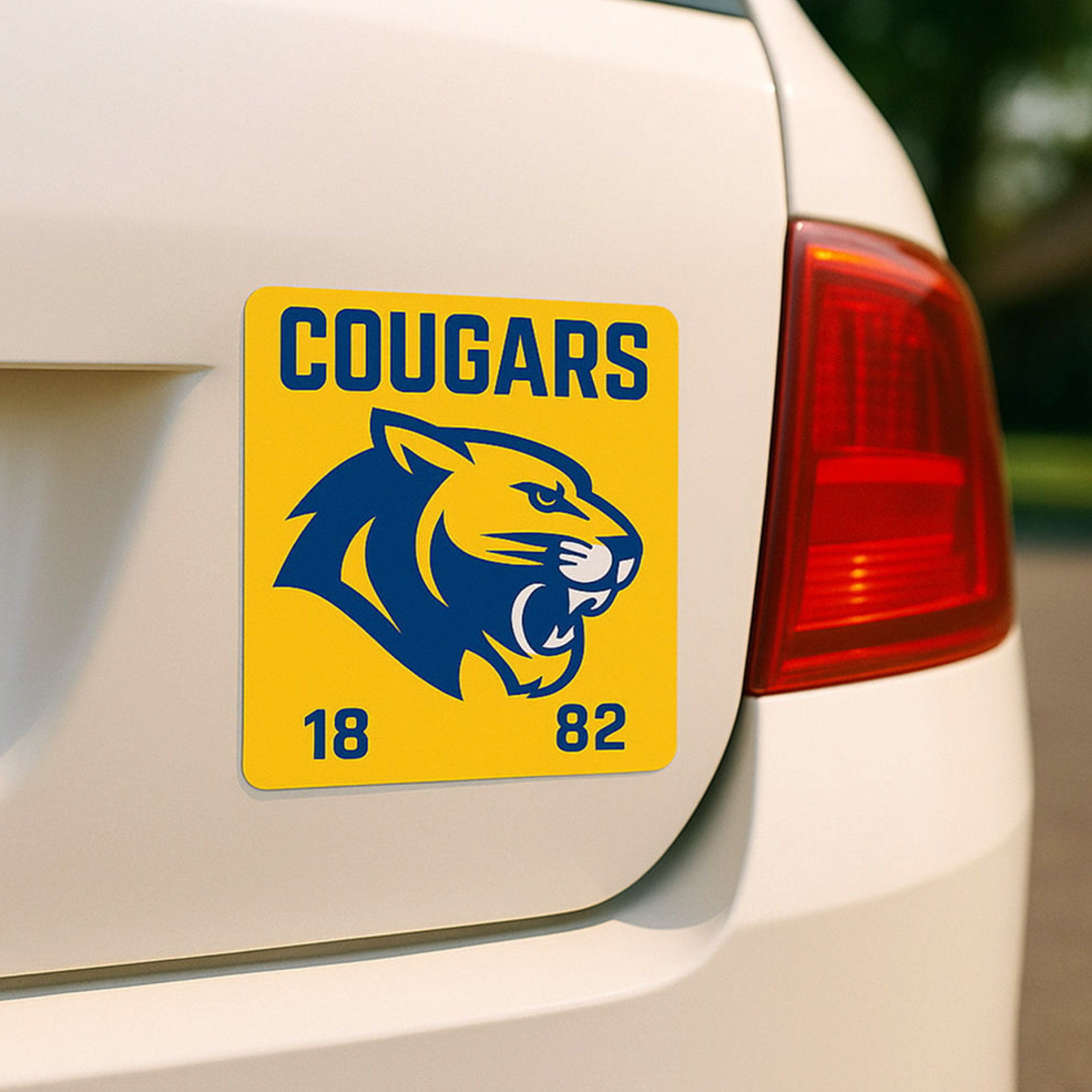 A square vehicle magnet features a blue cougar mascot with the text "COUGARS" and the year "1882." The weather-resistant magnet demonstrates custom magnets for schools, sports teams, alumni organizations, fundraising campaigns, and vehicle branding.