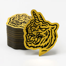 Stack of metallic gold and black tiger-themed stickers on a white background