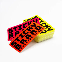 Stack of colorful stickers with NEON 'Sticky Brand Creative Group' text on a white background fluorescent