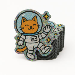 Stack of pixie dust glittery stickers with a cat in an astronaut suit design on a white background