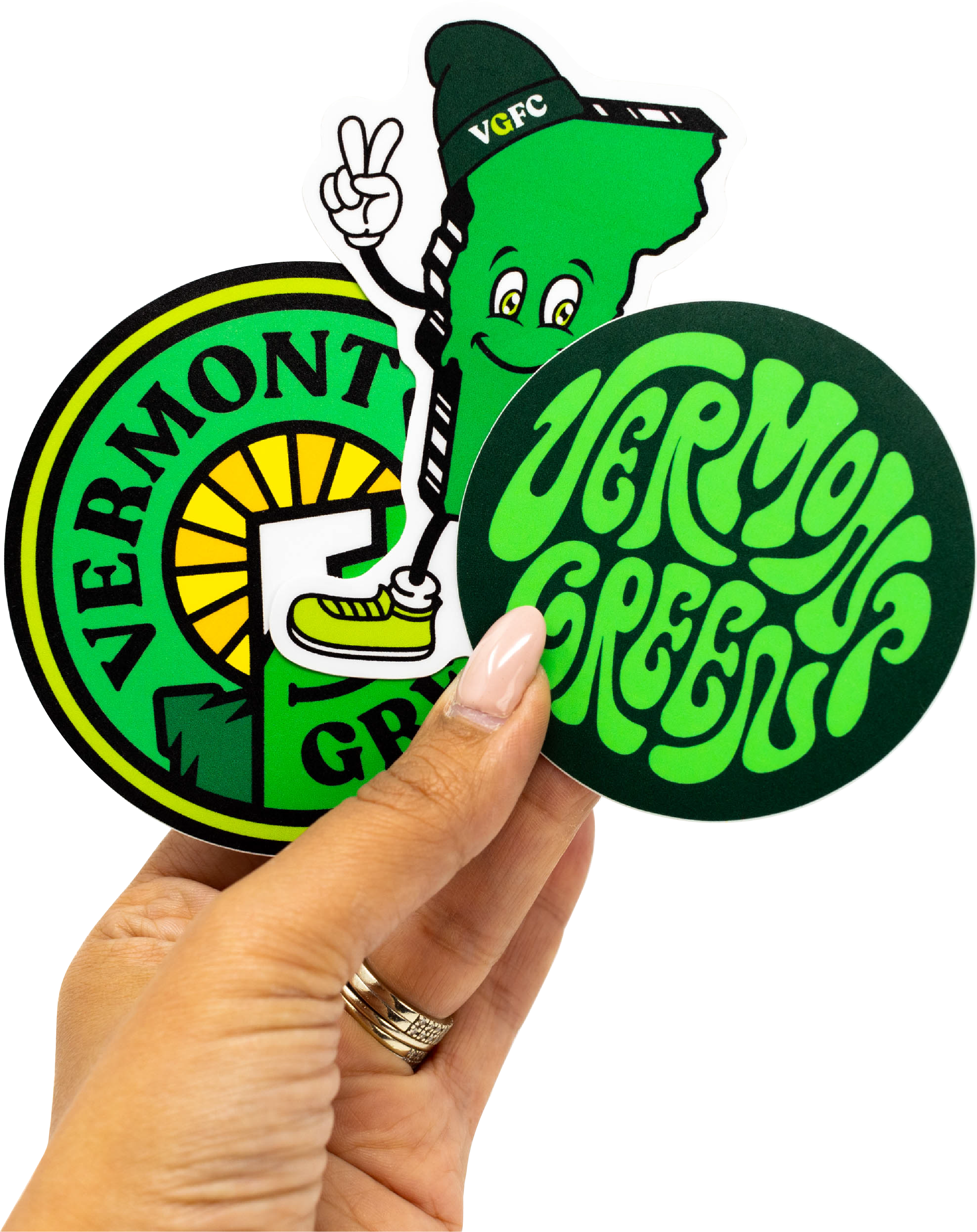 Two Vermont Green soccer club team stickers held by a hand, with one featuring a cartoon character and text. Vermont Green. VGFC.