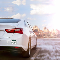 White Car driving towards city with oval sticker that reads 'Native Earth